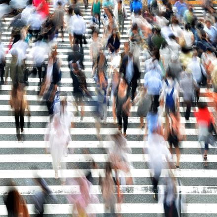 Blurred motion of a large crowd crossing a street in a busy city, emphasizing rapid movement and urban life.