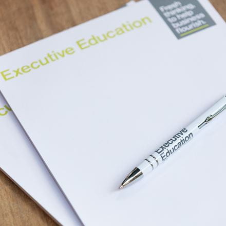 An Executive Education notepad and pen are laid upon a wooden desk