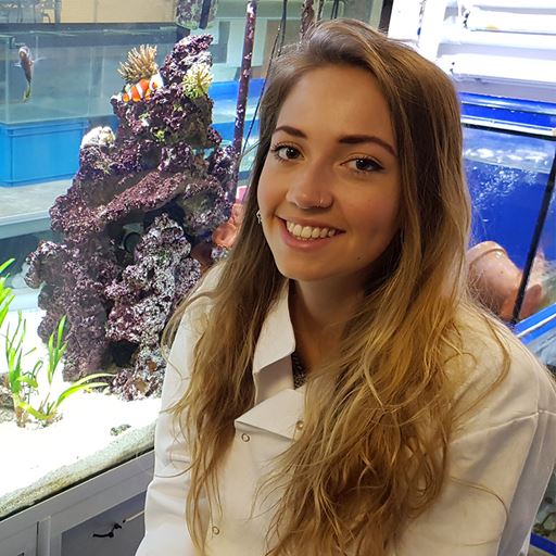 Harriet wearing a lab coat and sitting in front of a coral tank.