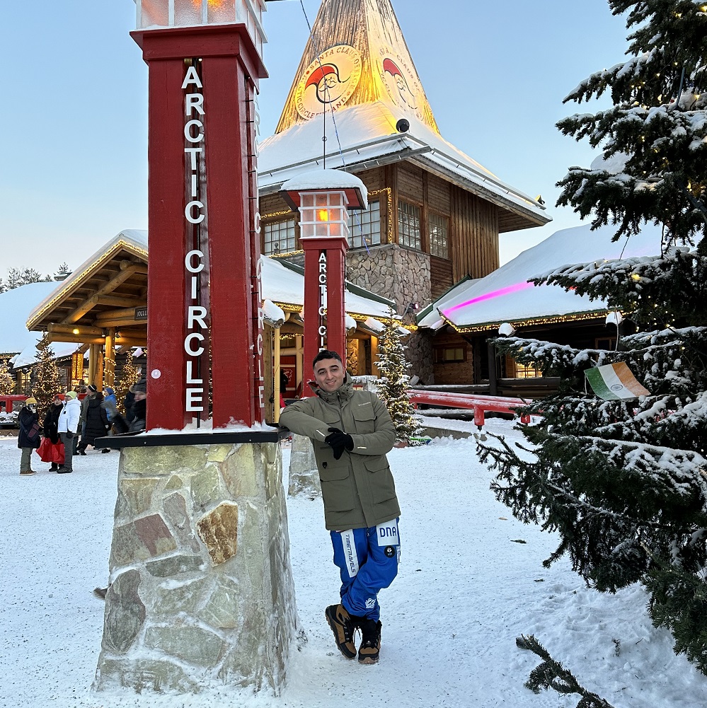 student stood in the snow in front of arctic circle sign