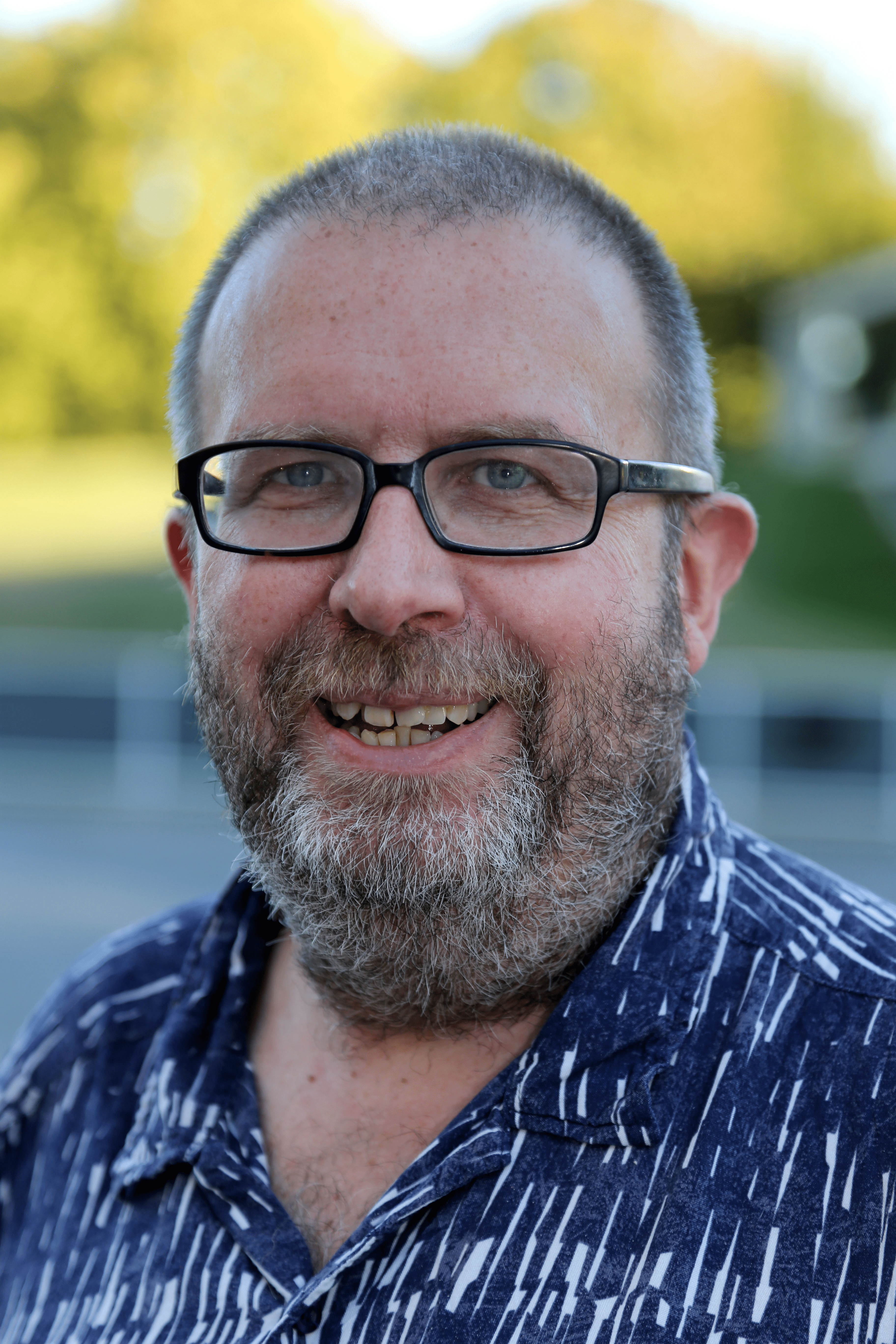 A portrait photograph of Professor John Preston, wearing a blue shirt, and black framed glasses