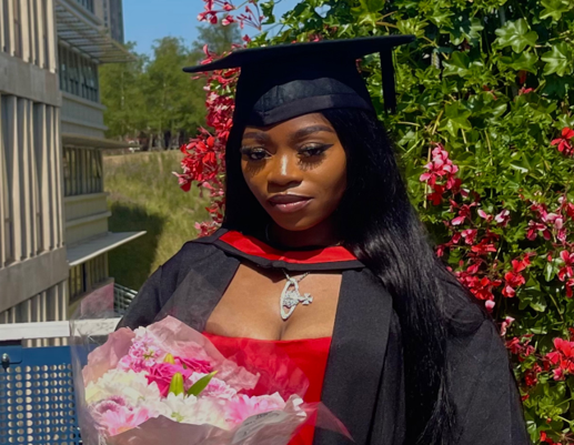Photo of Michelle smiling at camera, wearing a graduation gown and hat and holding flowers