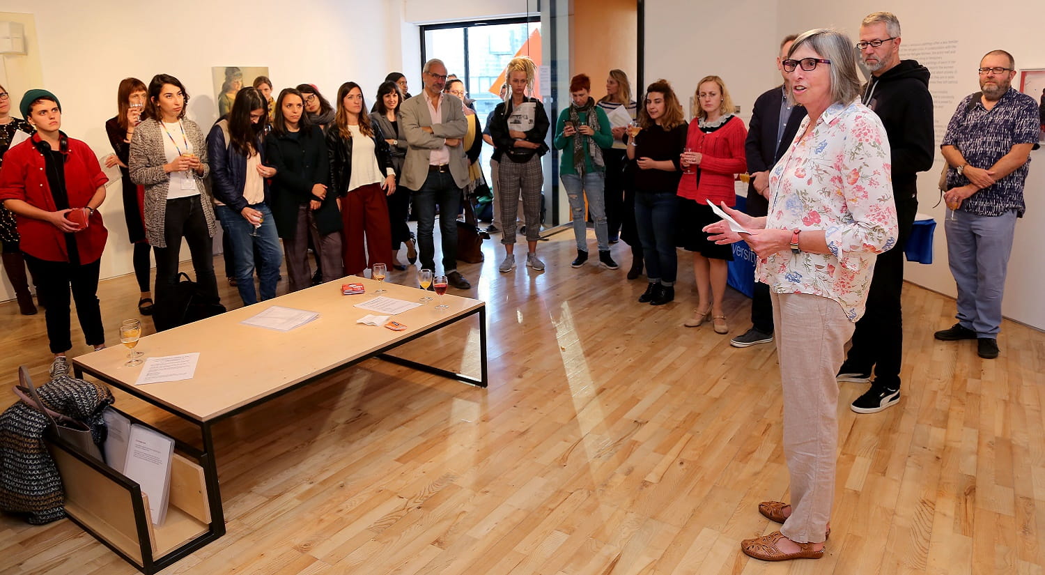 A crowd of people in a white room, watching a presentation being given by Pro-Vice Chancellor Christine Raines at the launch event for Centre for Migration Studies.