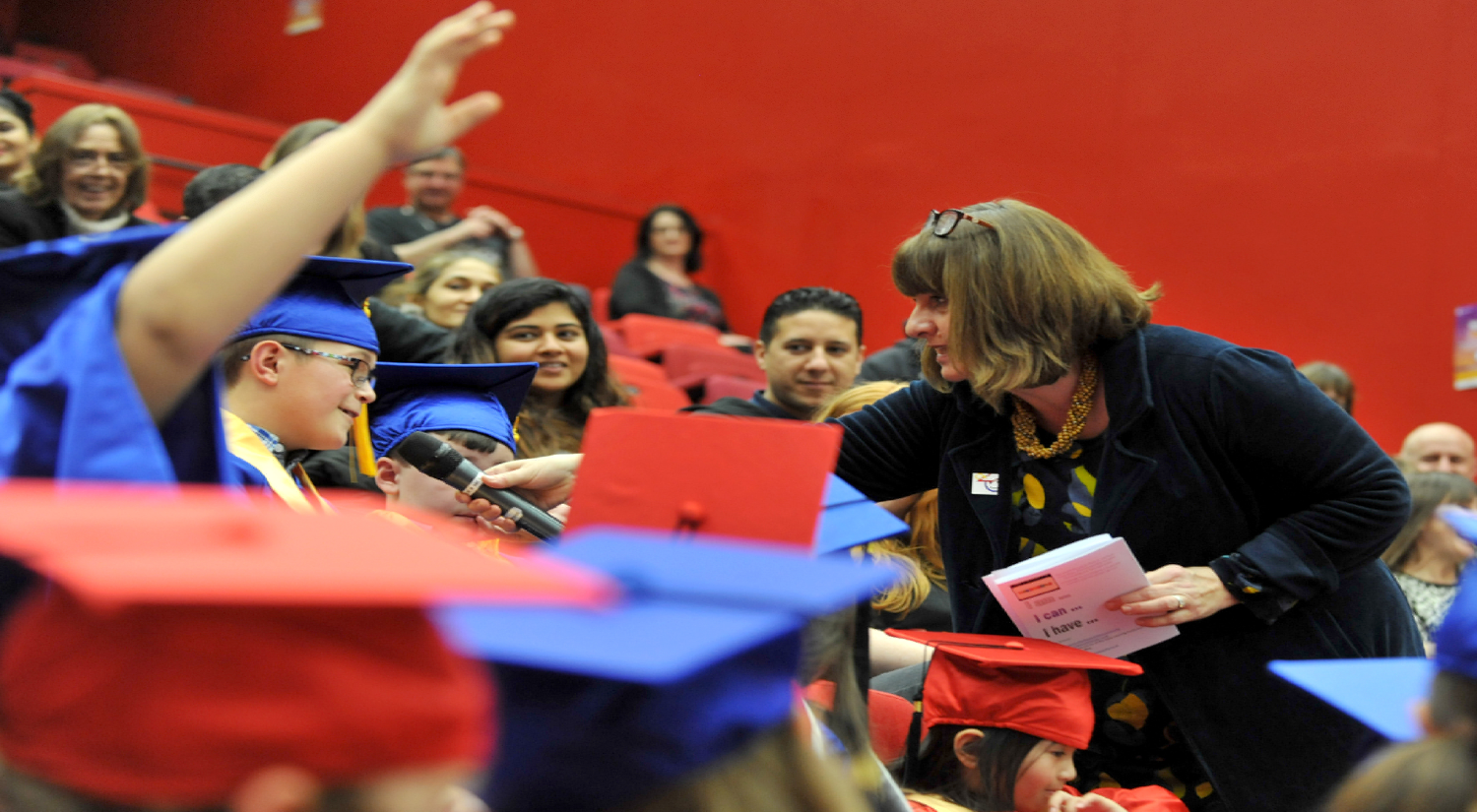 Adult woman holding microphone in front of young boy in audience to ask a question