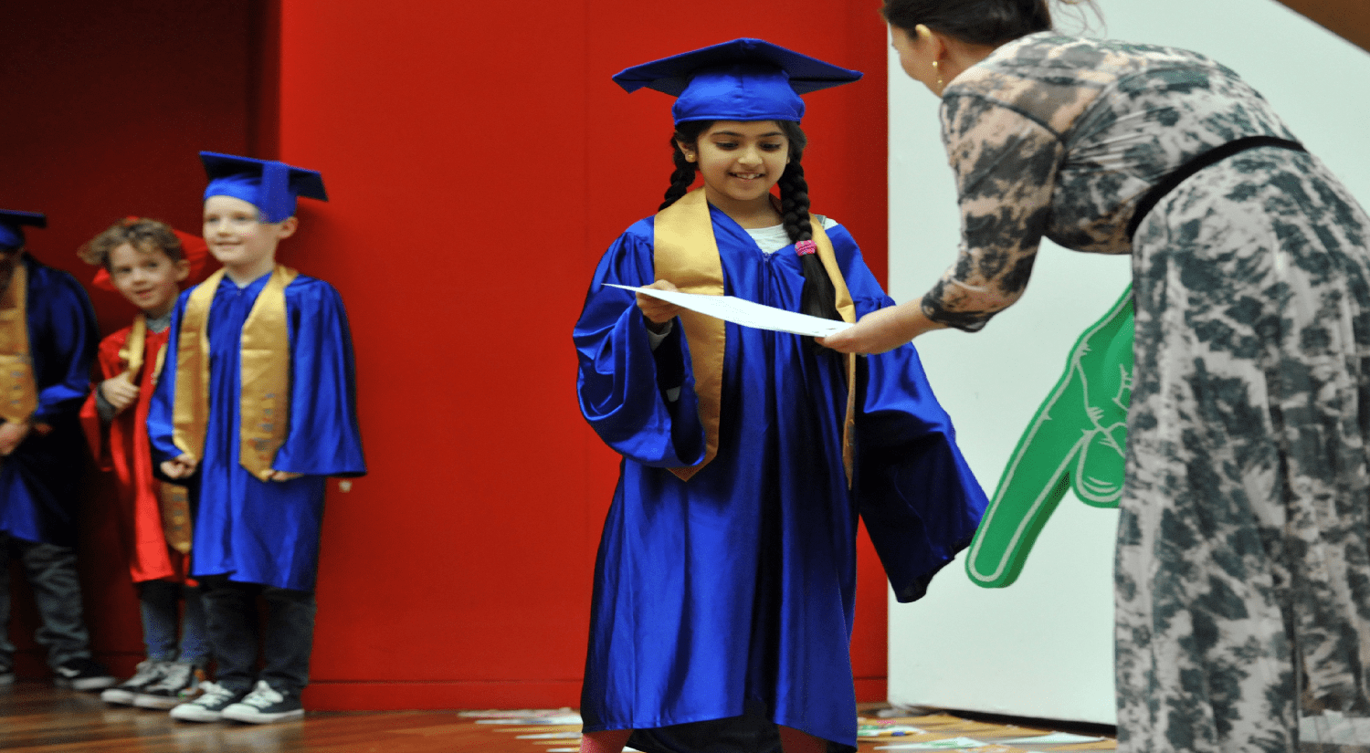 Young girl in blue gown receiving her children's university graduation certificate from the organiser
