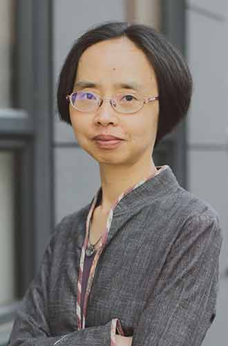 Dr Xun Zhou wearing wire-rimmed glasses and a grey jacket, with her arms folded