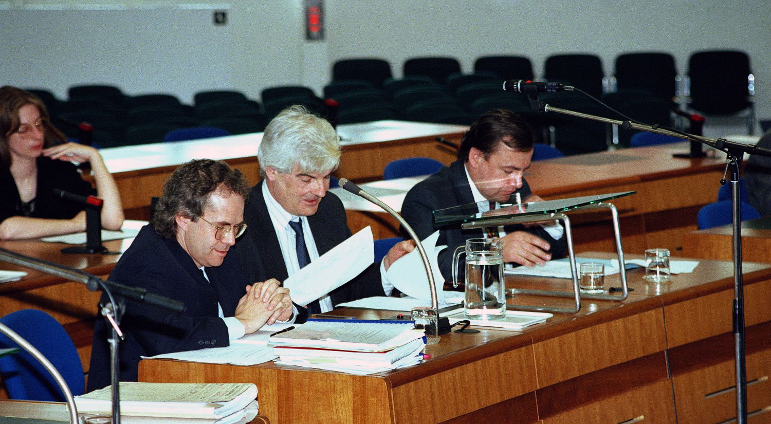 An old photo of three men with paperwork in a court room.