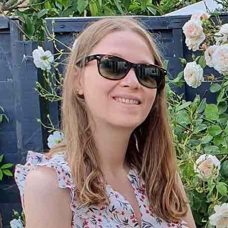 Hannah Onslow, smiling and wearing sunglasses, photographed in front of a rose bush