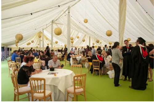 Graduation reception tent with people sitting at the tables while students celebrate