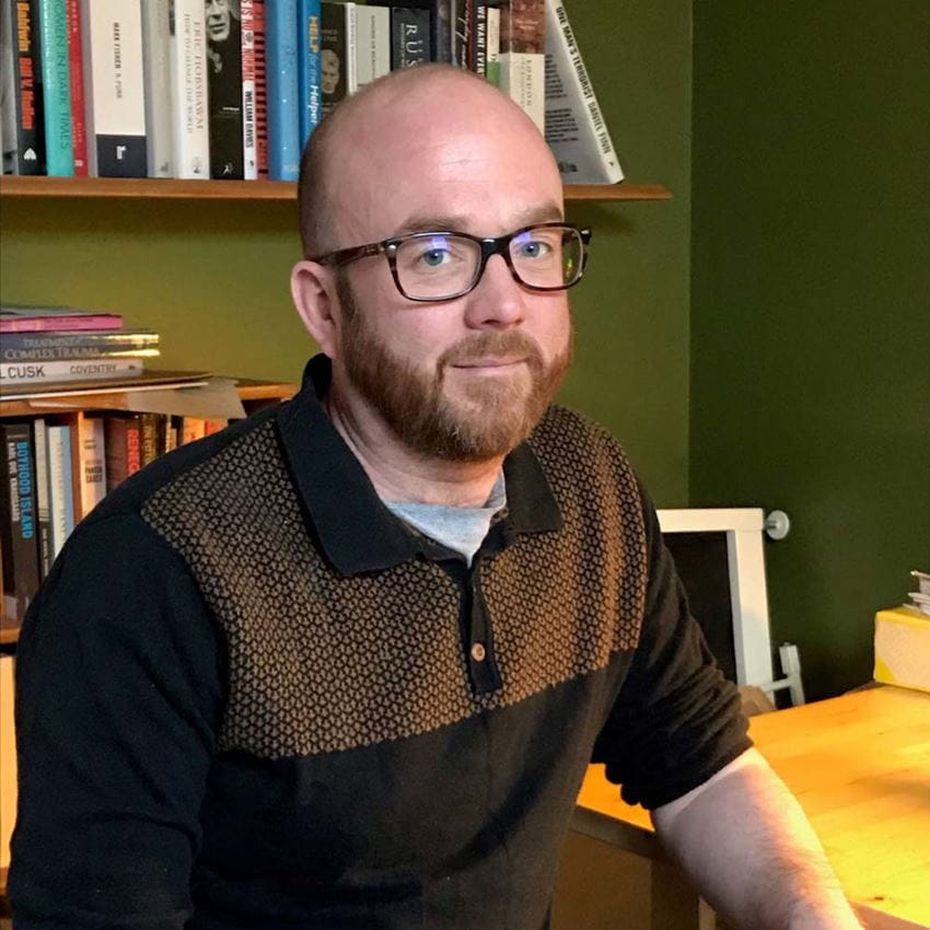 Dr Danny Taggart sitting a table smiling at the camera