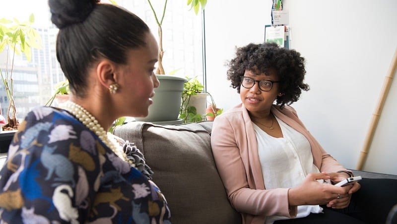 Two women on a couch talking.