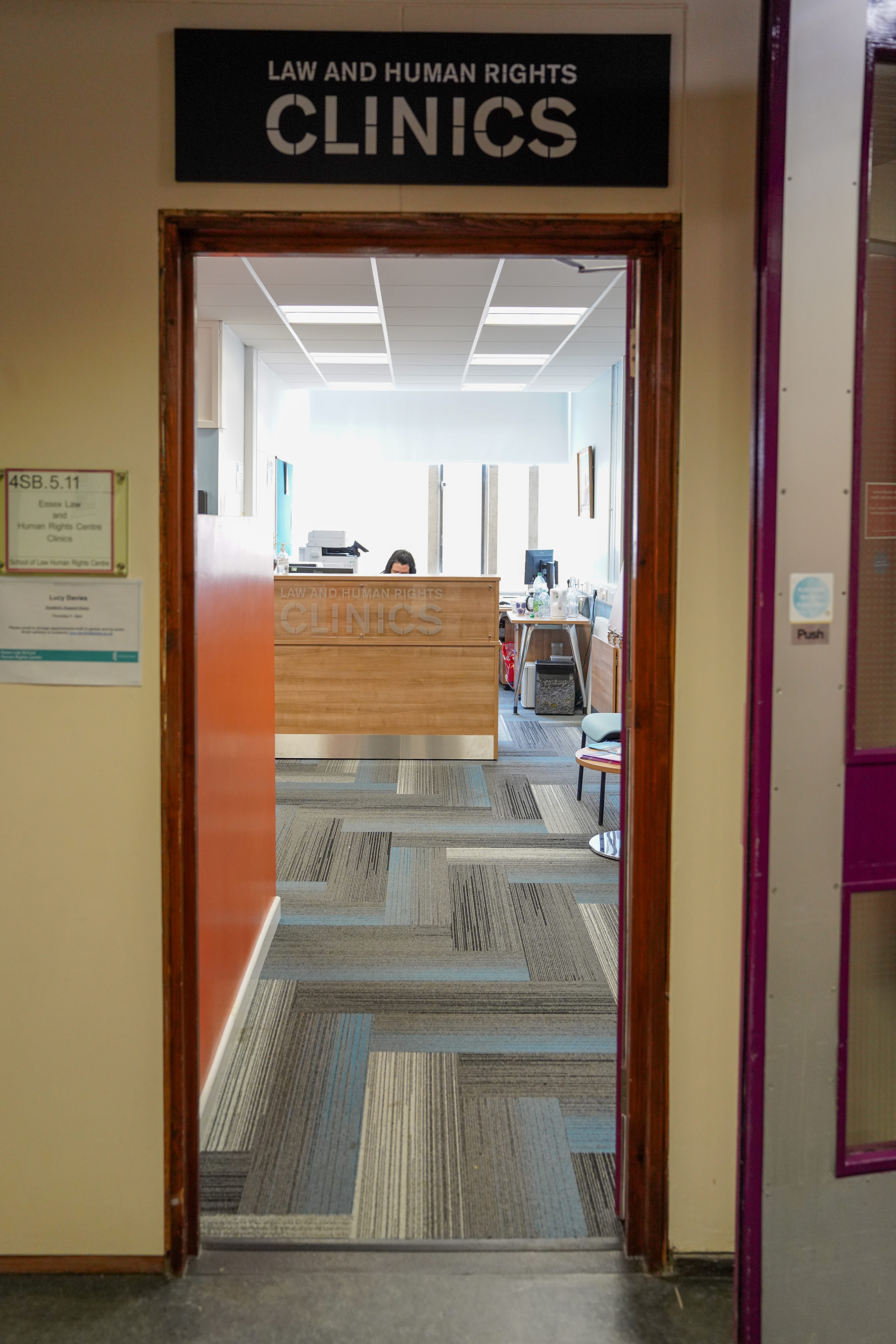 Picture of the front of the law clinic shows a door with a reception desk on the back ground. The lettering says "Law and Human Rights Clinic"