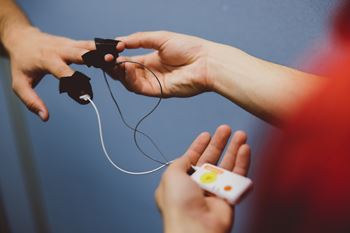 Close up of a lab assistant attaching electrodes to the tips of another person's fingers