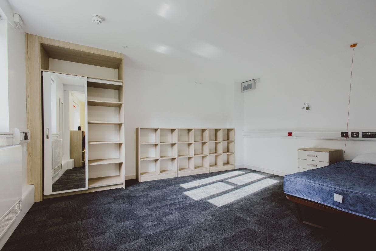 Large room with a bed, wardrobe, shelving and call points