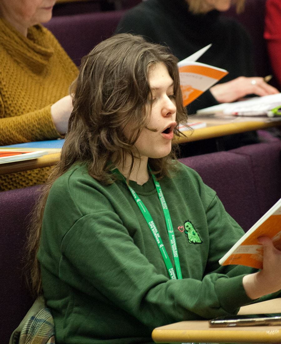 Member of the UoE Choir singing from their sheet music