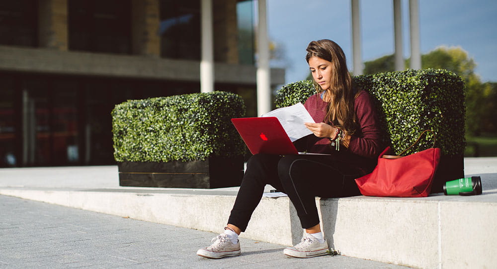 A girl sitting outside the Silberrad Student Centre on her laptop
