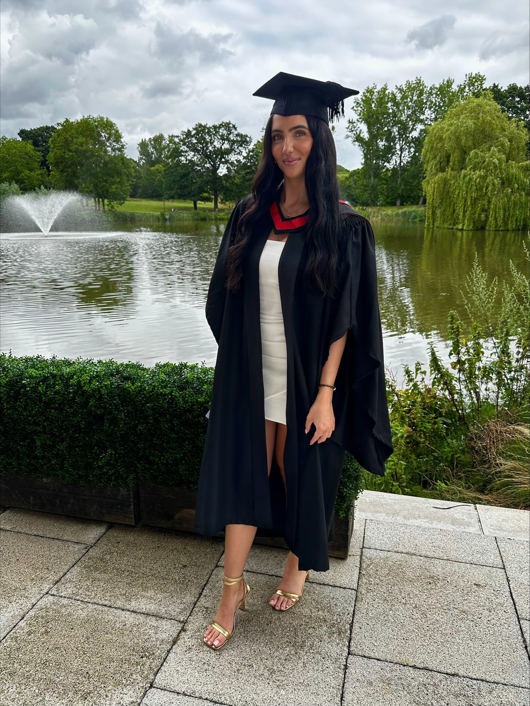 Student Leila in a graduation gown standing in front of a lake