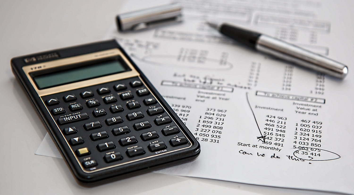 A calculator and a spreadsheet on a desk with a pen.