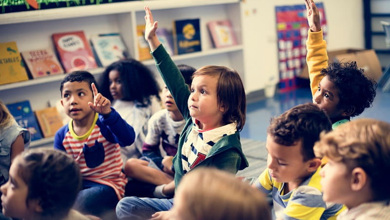 Primary school children in a classroom with their hands up