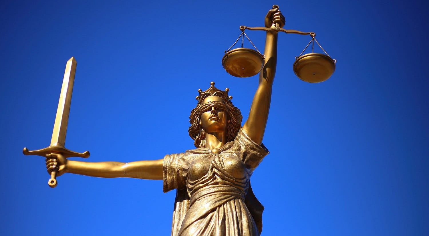 A bronze statue of justice with a clear blue sky in the background.