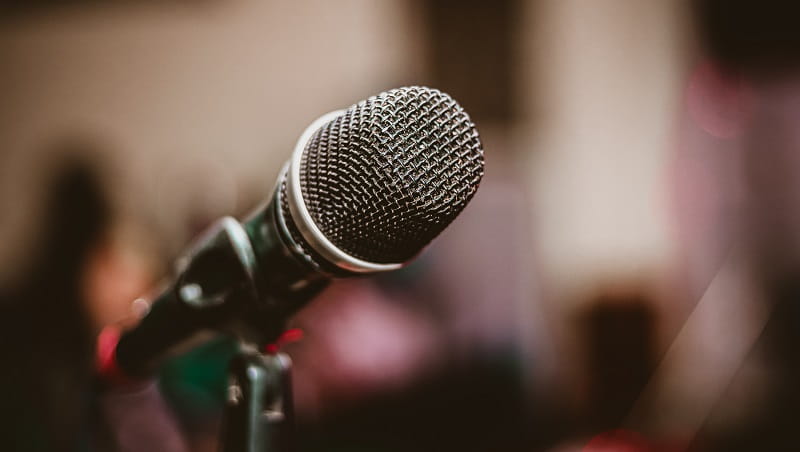 A close up of a microphone with a blurred crowded room in the background.