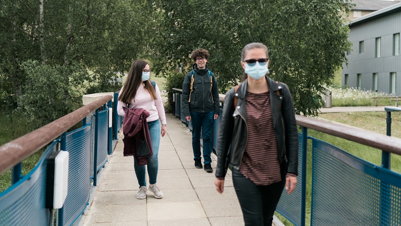 Students walking across a bridge in Colchester campus and wearing face masks.