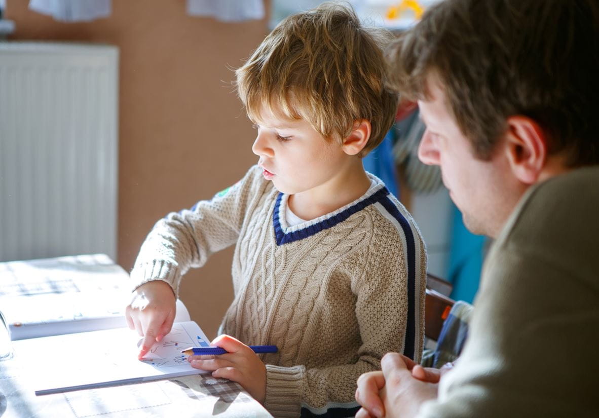 A young child in primary school learning from a book with guidance from a teacher.