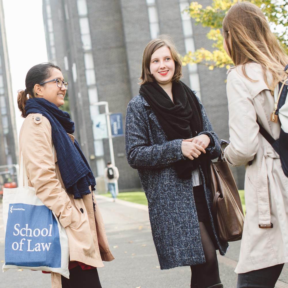 Essex students talking outside the North Towers at Colchester Campus holding a Tote Bag with the Department of Law emblazoned on it
