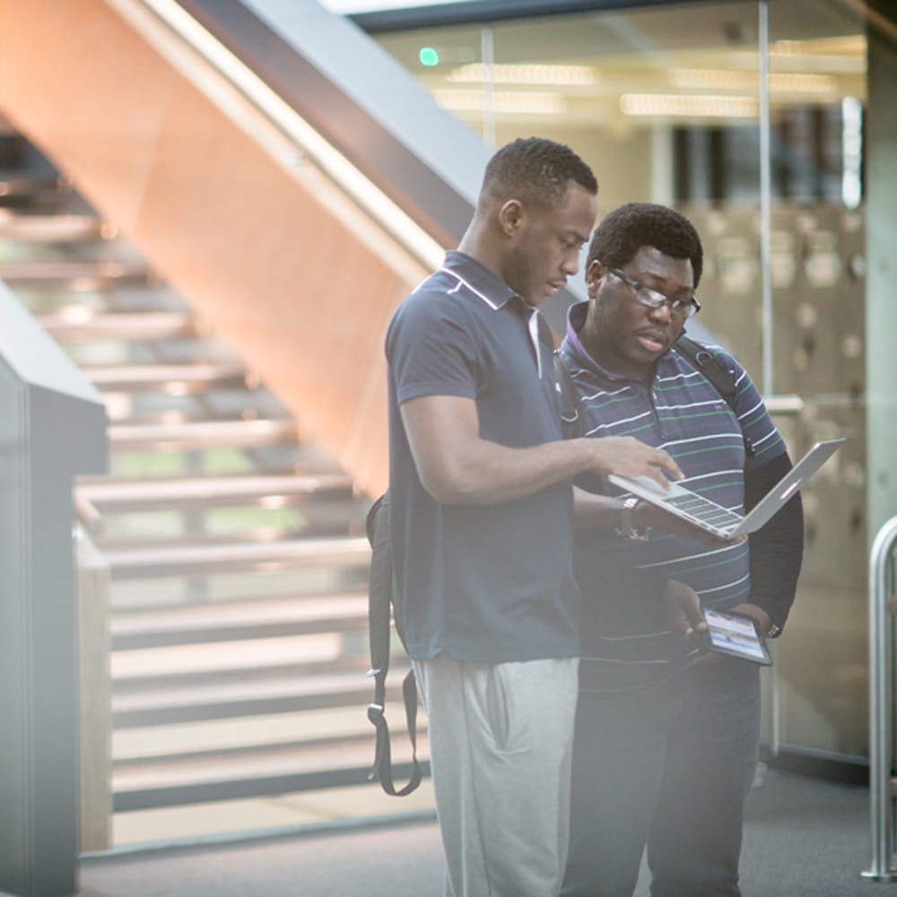 Two students looking at a laptop at the bottom of stairs in Southend