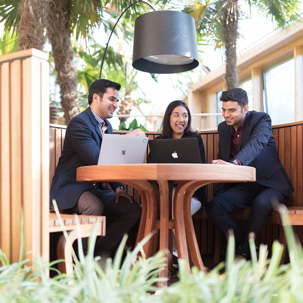Three MBA students sit around a table in the Winter Garden in discussion 