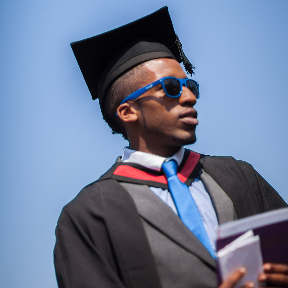 Photo taken from below of a male graduate wearing sunglasses and his robes at graduation.