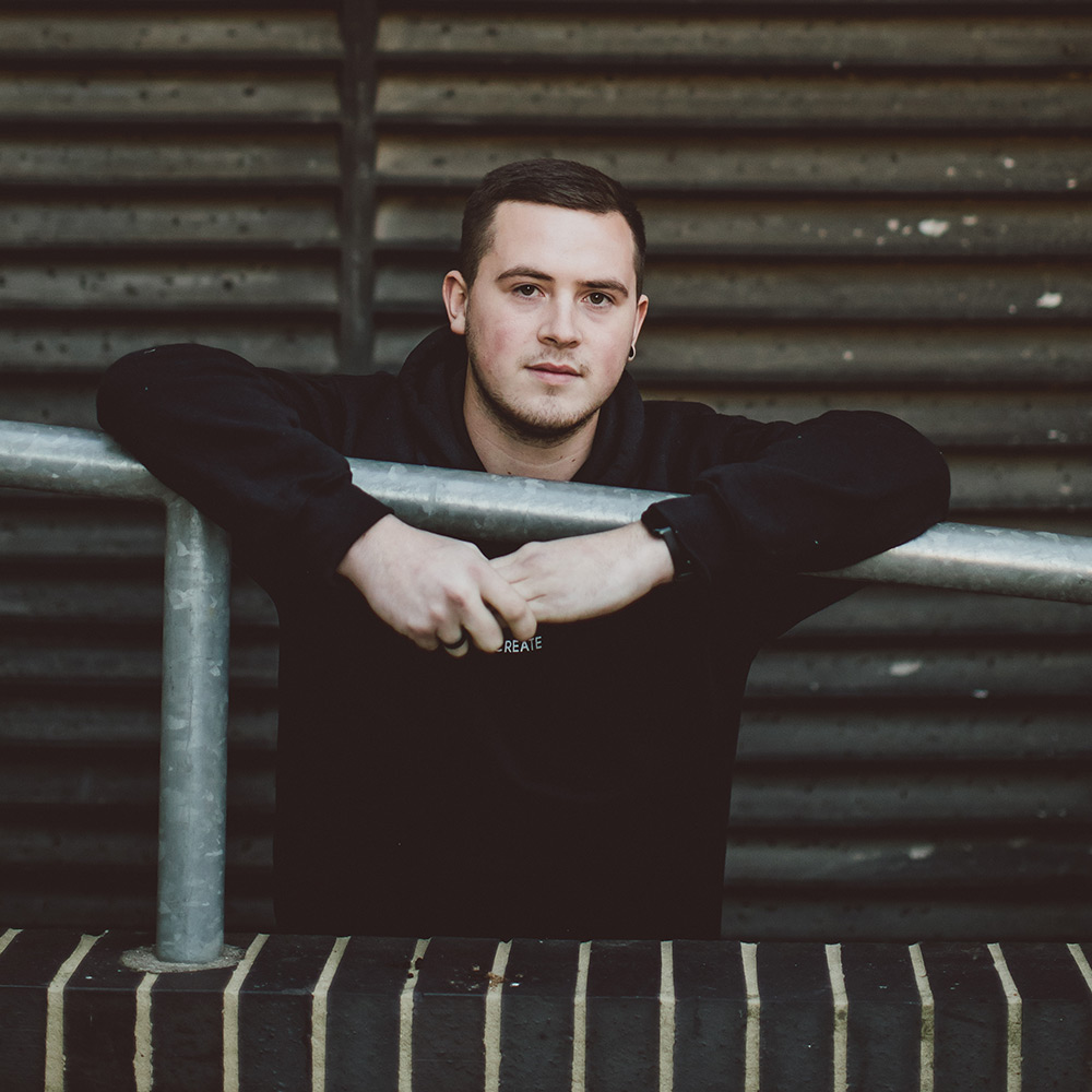 Jake leaning over a railing wearing a black hoodie.