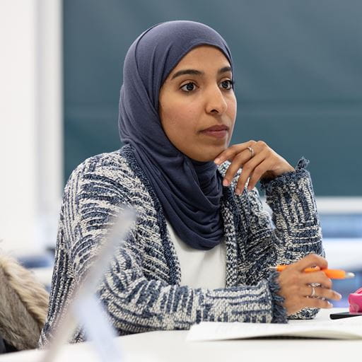 An Essex Business School student wearing a blue hijab headscarf sits in a classroom with a pen in her hand.