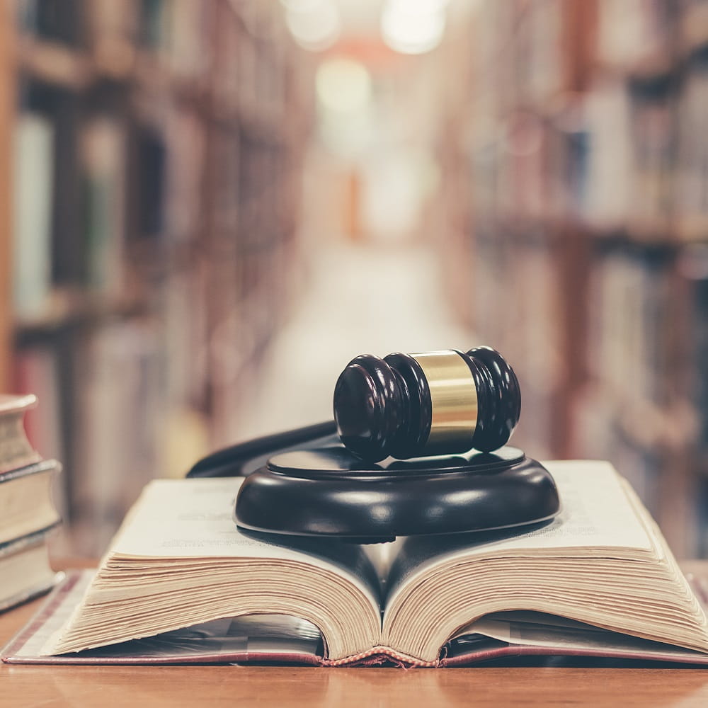 A gavel on top of an open book with a library in the background.