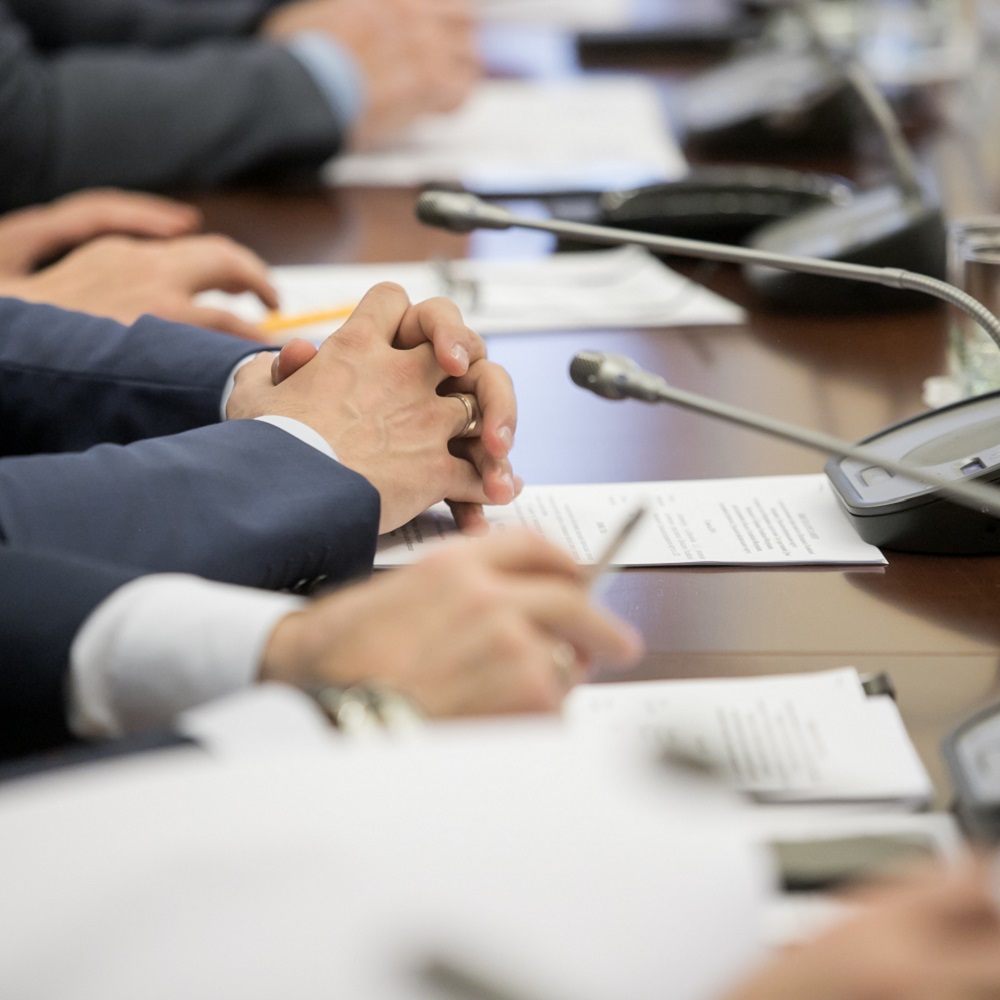 A row of people sat at a table at political summit with microphones and papers on the desk