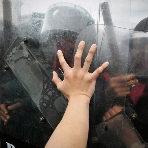 A persons arm pushed up against riot shields with police behind them.