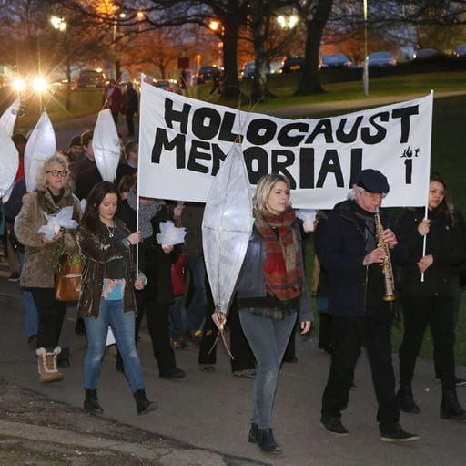 Procession of people with lanterns holding a handmade banner which says Holocaust Memorial