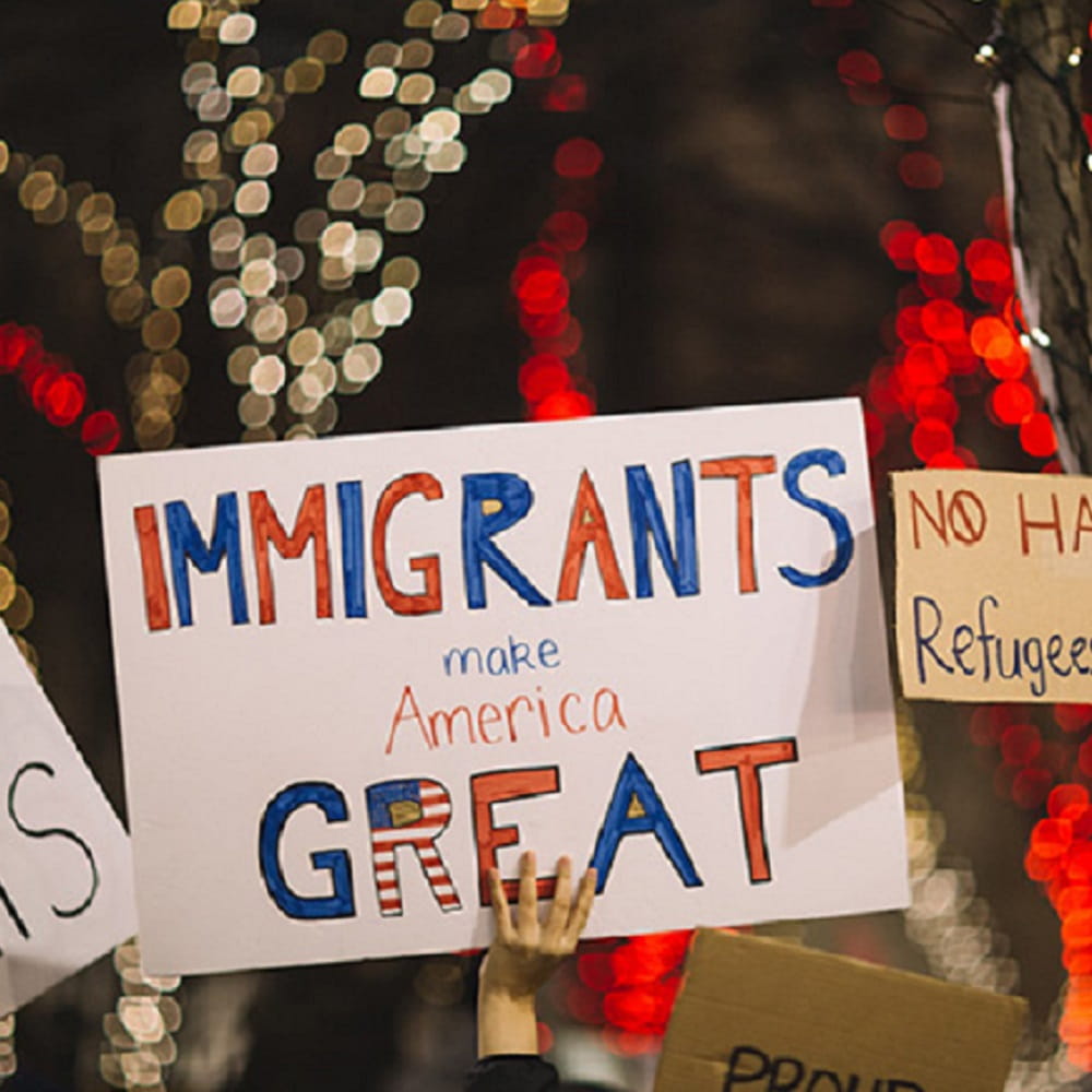 A protesting crowd holding up placards which say 'immigrants are what make America great'.