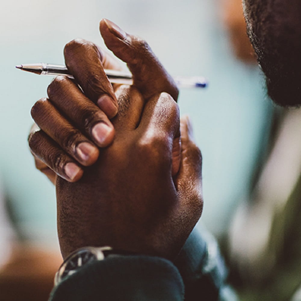 A student clasping their hands and holding a pen.