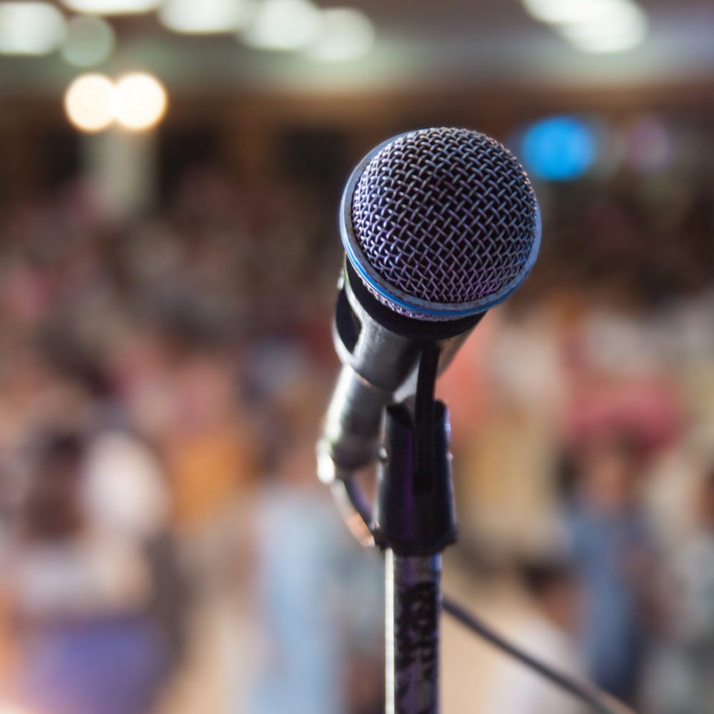 A close up of a microphone with a busy conference room in the background.