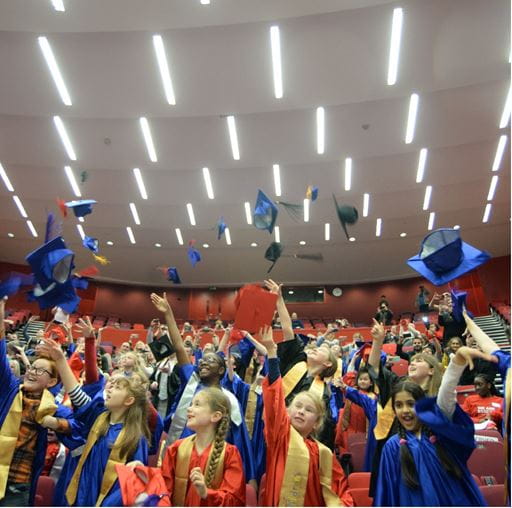 Primary school children attending graduation ceremony and throwing mortar boards in the air