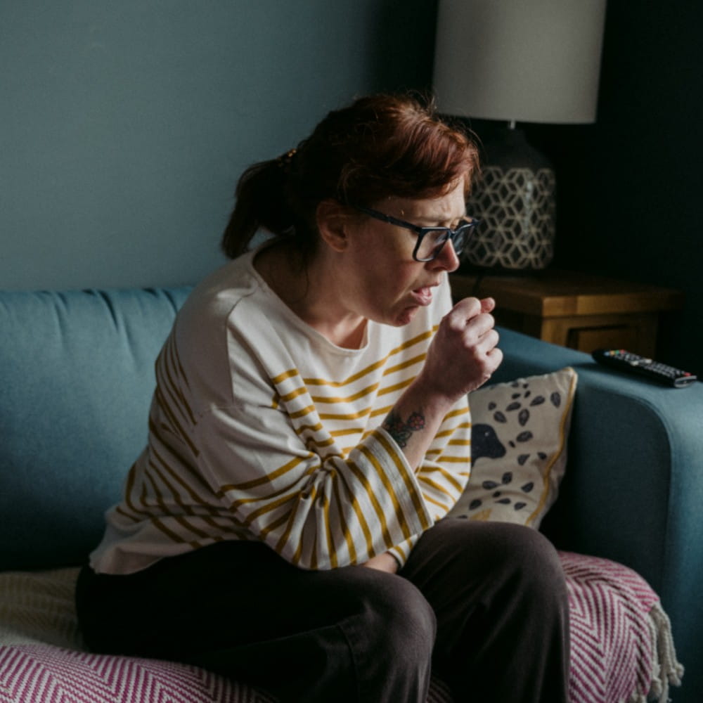 coughing woman sat on sofa