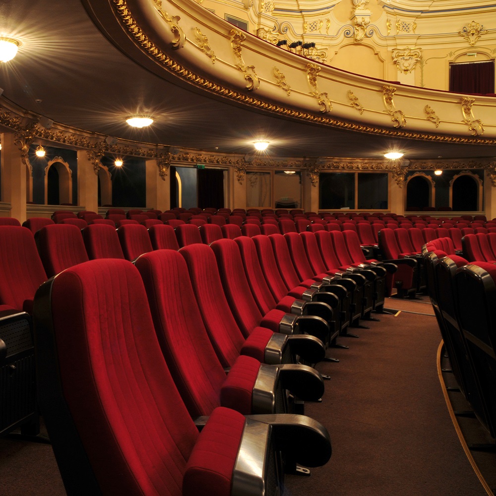A row of empty red velvet theatre seats.