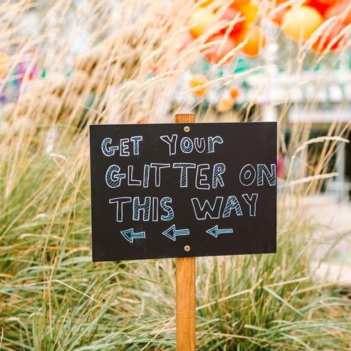 Black chalk sign saying "get your glitter this way"