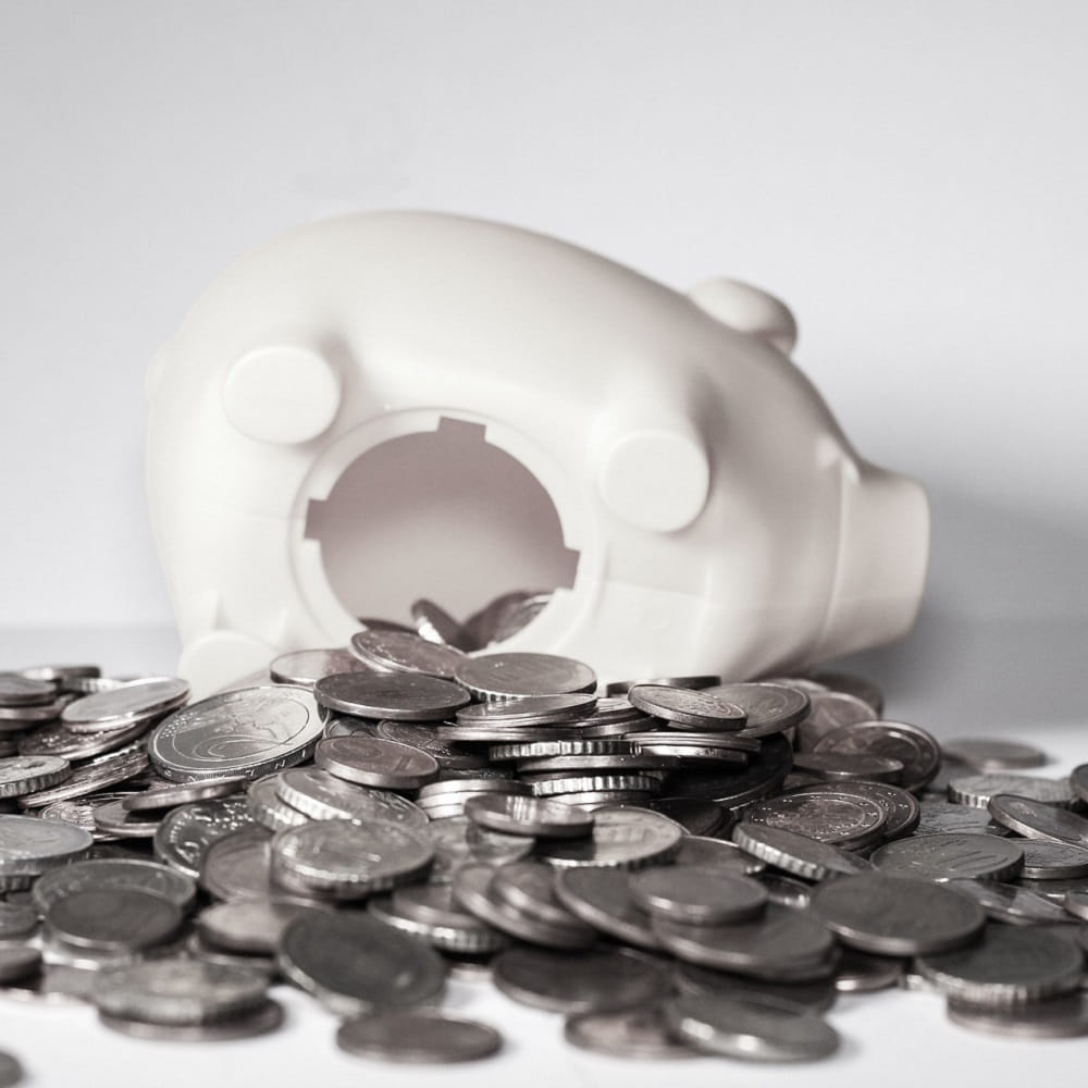 A white ceramic piggy bank turned upside down with coins everywhere.