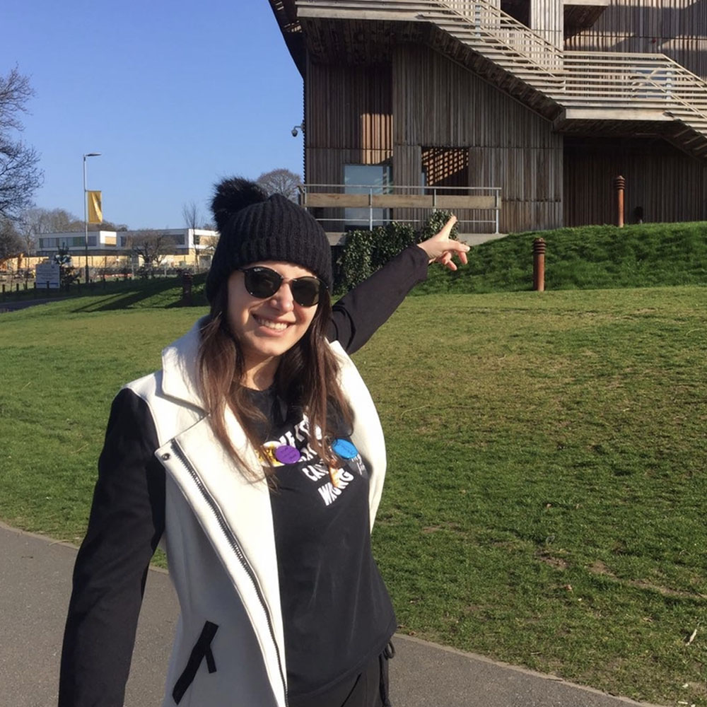 Young lady casually dressed pointing to Essex Business School building 