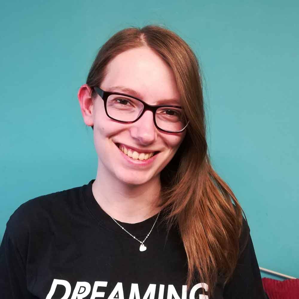 Amanda Horne, wearing a black t-shirt and glasses, against a teal-coloured wall 