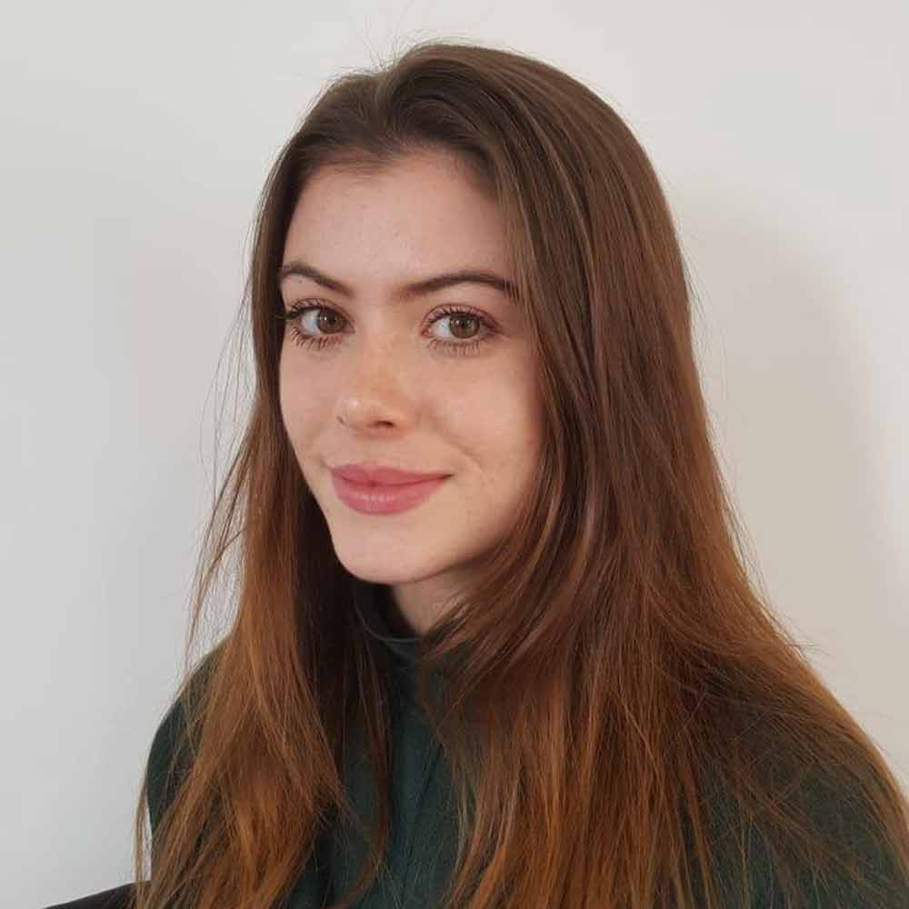 Holly Worrall, wearing a black top and standing against a white wall