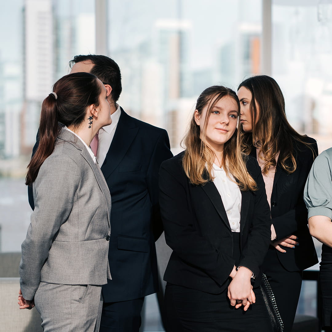 A smiling student stands, focusing on someone else talking.