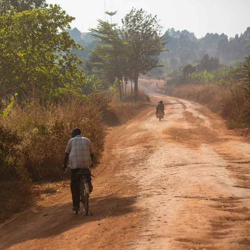 A dirt road in Uganda with cyclist travelling away into the distance.